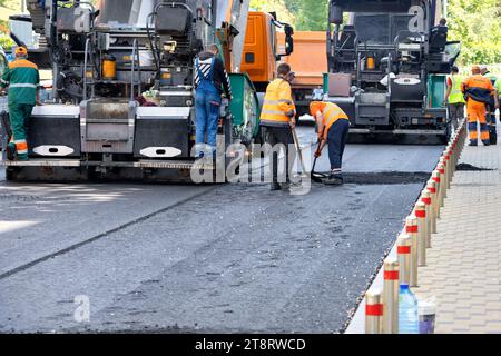 Straßenarbeiter legen an Sommertagen mit großen Industrieblättern Asphalt auf einer Stadtstraße ab. Kopierbereich. Stockfoto