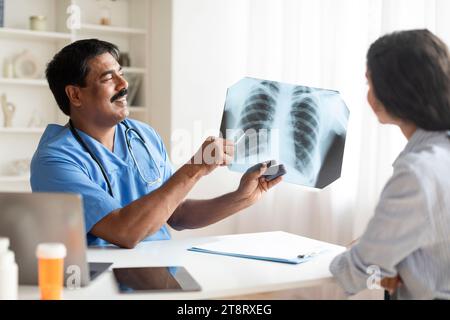 Indischer Doktor Mann demonstriert Thoraxröntgenaufnahme bei weiblicher Patientin in der Klinik Stockfoto