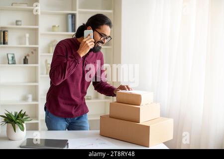 Kleine Unternehmen. Indischer Mann, Der Bestellungen Packt Und Zu Hause Telefoniert Stockfoto