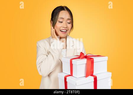 Überrascht fröhliche junge chinesin feiert Feiertag, sehen Sie sich viele Geschenke an Stockfoto