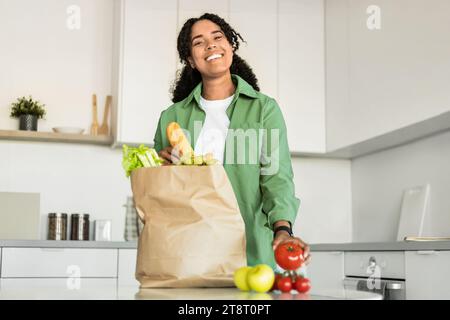 Die schwarze Dame packt Lebensmittellieferungen aus und posiert mit einer Papiertüte drinnen Stockfoto
