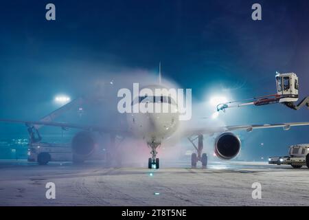 Enteisung des Flugzeugs vor dem Flug. Winter frostige Nacht- und Bodenservice am Flughafen bei Schneefall. Stockfoto