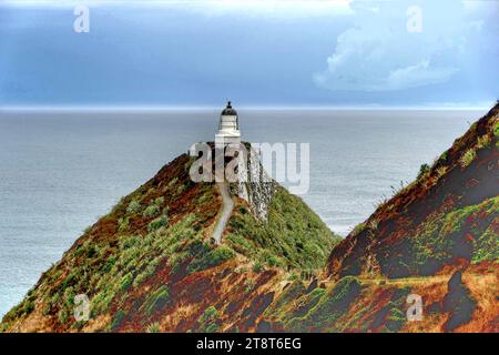 Leuchtturm Nugget Point. Otago, der berühmte Nugget Point (oder „die Nuggets“, wie von den Einheimischen genannt), befindet sich in der Nähe von Kaka Point. Es gibt einen Parkplatz, von wo aus Sie Ihren Spaziergang zum Nugget Point Lighthouse beginnen. Von der Aussichtsplattform am Ende des Weges aus sind wellenerodierte Felsen zu sehen, die mit der Form von Goldnuggets verglichen werden. Der Leuchtturm wurde 1869–70 erbaut, ist 9,5 Meter hoch und liegt 76 Meter über dem Meeresspiegel Stockfoto