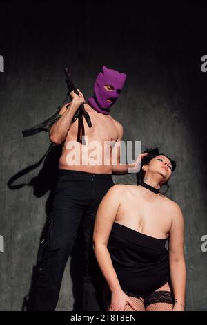 Ein Mann, der eine Maske mit einem Maschinengewehr trägt, mit einer Frau im Kragen Stockfoto