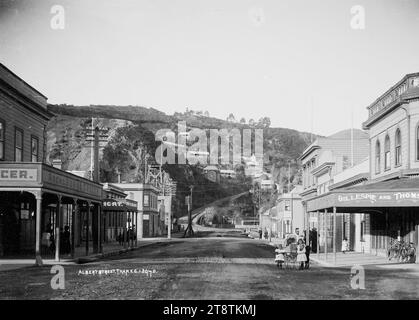 Blick auf die Albert Street, Themse, Blick auf die Albert Street zu Häusern auf dem Hügel über der Upper Albert Street. Auf der linken Seite der Straße im Vordergrund befinden sich die Räumlichkeiten von Archibald Burns, Lebensmittelhändler. Auf der gegenüberliegenden Straßenseite (an einer Kreuzung) befinden sich die Räumlichkeiten von Gillespie & Burns. Zu erkennen sind die Gebäude weiter die Straße hinunter das Queen's Hotel (F Grubb) und am Ende der Straße das Büro des Evening Star. Im Vordergrund stehen auf der Straße und schauen auf den Fotografen zwei kleine Mädchen und ein Junge mit Kinderwagen. Stockfoto