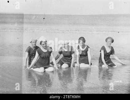 Im Meer baden, fünf unbekannte junge Frauen sitzen zusammen im flachen Wasser am Strand. Sie tragen alle Badesachen und Mützen. Der Ort ist nicht bekannt. Anfang der 1900er Jahre Stockfoto