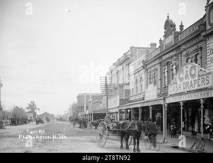 The Square, Palmerston North, Blick nach Süden in Richtung Manawatu Stables, Blick auf den Platz mit einer Reihe von Geschäften auf der rechten Seite, einschließlich der Geschäftsräume von Collinson & Cunninghame (Leopold H Collinson und John Cunninghame, Geldautomaten), Robert S Barry (Importeur) und Leopold Simmons (Draper) im Vordergrund. Die Gebäude der Manawatu Stables befinden sich am Ende des Platzes und es gibt mehrere Pferdewagen auf der Straße Stockfoto