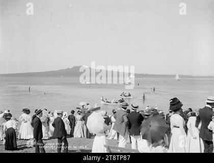 Menschenmenge am Cheltenham Beach, Devonport, Blick auf eine Menschenmenge am Cheltenham Beach, die mit dem Rücken zur Kamera steht und den Beginn eines Yachtrennens beobachtet. Das Startboot kann in der mittleren Entfernung gesehen werden (mit der Insel Rangitoto dahinter). Mehrere Ruderboote befinden sich in der Nähe der Küste. Anfang der 1900er Jahre Stockfoto