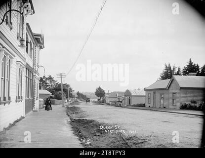 Blick auf Queen Street, Northcote, Auckland, Neuseeland, Blick auf Queen Street, Northcote, stehend vor der Northcote Tavern mit Blick auf das Meer in der Ferne. Häuser und Holzgebäude sind auf beiden Seiten der Straße zu sehen. Eine Frau läuft auf dem Fußweg vor der Taverne zur Kamera. Ein Pferdebus ist in der Entfernung um 1910 zu sehen Stockfoto