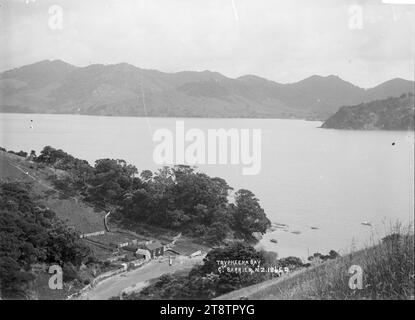 Blick hinunter auf Tryphena Bay, Great Barrier Island, Blick hinunter auf die Bucht von einem hohen Aussichtspunkt. In der Nähe des Ufers sind Scheunen und Werften zu sehen, und in der Bucht sind Jollen verankert. Anfang der 1900er Jahre Stockfoto