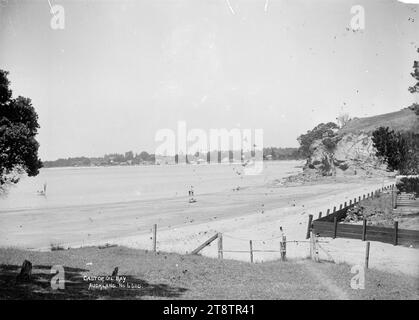 Castor Bay, Auckland, Neuseeland, Blick von der Mitte des Strandes in Richtung Milford Beach im Süden. Zwei Männer stehen am Ufer und eine Jacht nähert sich dem Ufer. Anfang der 1900er Jahre Stockfoto