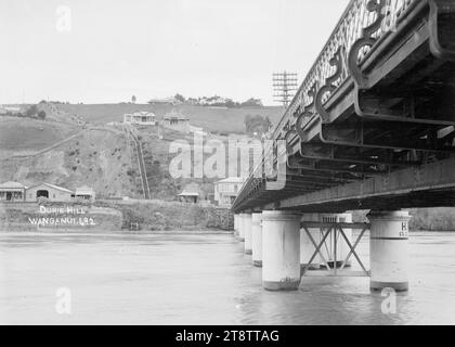 Blick auf Durie Hill mit einem Teil der Brücke, die den Wanganui überquert, New Zealand River, der von Durie Hill zur Victoria Avenue führt, Blick auf Durie Hill, aufgenommen unter der Brücke, die von der Victoria Avenue nach Durietown führt. Auf der anderen Seite des Whanganui River sind die Geschäftsräume von Gordon's Stables und Henley Sadler sichtbar Stockfoto