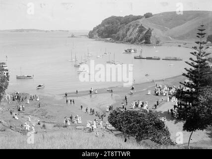 Home Bay, Motutapu Island, Foto um 1910 von William Price. Allgemeiner Blick auf Home Bay, Motutapu Island, von einem Hügel am nördlichen Ende des Strandes aus, der nach Süden in Richtung Motuihe Island in der Ferne blickt. Es gibt viele Boote in der Bucht, einschließlich einer Fähre, und Menschenmassen am Strand Stockfoto