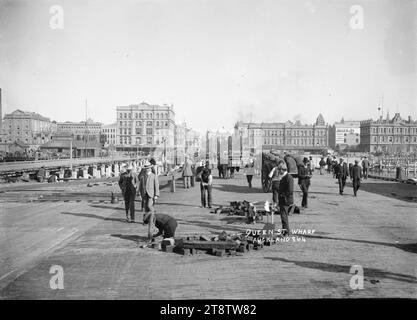 Queen Street Wharf, Auckland, Neuseeland, zur Zeit der Ersetzung der alten Queen Street Wharf durch eine neue Ferrobeton-Anlegestelle. Blick direkt auf die Queen Street mit Endeans Building (erbaut 1905) auf der linken Seite und Gladstone Building (erbaut 1883) mit Gladstone Coffee Palace auf der rechten Seite. Ganz rechts befindet sich der Hauptsitz des Auckland, New Zealand Harbour Board; alle in der Quay Street. Auf der linken Seite werden neue Betonpfähle in das Hafenbett getrieben. Im Vordergrund ersetzen Arbeiter Holzblöcke auf dem alten Kai. Stockfoto