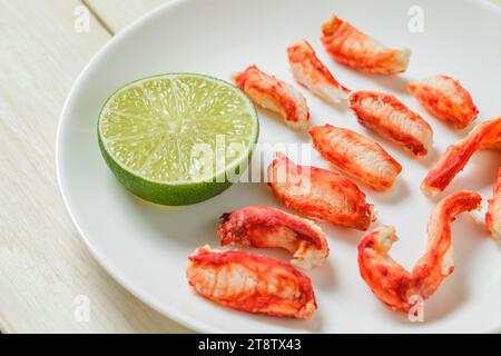 Krabbenfleischscheiben und Limette auf Platte auf weißem Holzbrett Hintergrund, selektiver Fokus Stockfoto