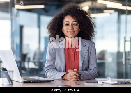Porträt der jungen schönen lächelnden Geschäftsfrau am Arbeitsplatz im Büro, Frau im Business-Anzug lächelt und in die Kamera schaut, weibliche finanzielle W Stockfoto