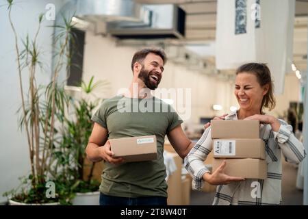 Zwei Kollegen, die Spaß beim Tragen von Kartonschachteln haben Stockfoto