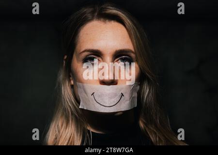 Missbrauch und häusliche Gewalt. Traurige depressive Frau versteckt ihren Mund hinter einem gefälschten Lächeln auf Papierband. Depression und psychische Gesundheit Stockfoto