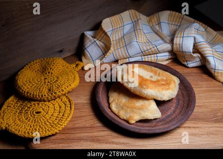 Tonplatte mit zwei einzelnen gebratenen Pasteten mit Fleisch auf Holztisch. Tatarische traditionelle Pasteten. Stockfoto