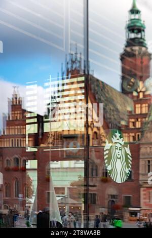 Das Starbucks-Logo auf dem Café-Fenster mit der verschwommenen Reflexion des Breslauer Rathauses in Breslau, Polen Stockfoto