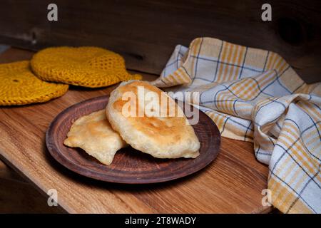 Tonplatte mit zwei einzelnen gebratenen Pasteten mit Fleisch auf Holztisch. Tatarische traditionelle Pasteten. Stockfoto