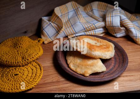 Tonplatte mit zwei einzelnen gebratenen Pasteten mit Fleisch auf Holztisch. Tatarische traditionelle Pasteten. Stockfoto