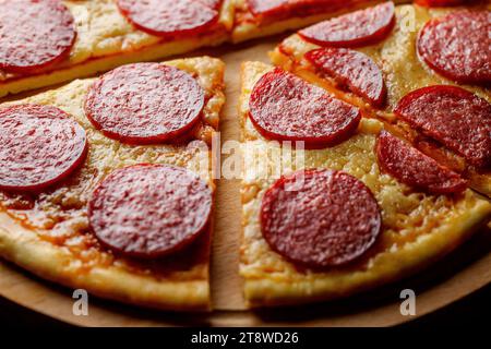 Pepperoni-Pizza in Stücke geschnitten auf Holzständer, selektiver Fokus. Stockfoto