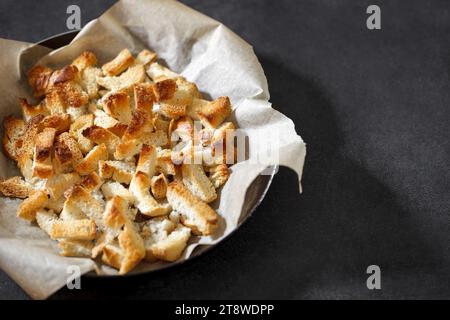 Cracker, trocken gebackene Stücke von weißem Brot, in der Pfanne mit Bastelpapier auf dunklem Hintergrund, selektiver Fokus. Stockfoto