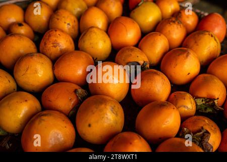 Reife orangefarbene Persimmonen. Auf dem Tisch auf dem Markt. Ein Haufen Bio-Persimmon-Früchte auf einem lokalen Bauernmarkt in Dalat, Vietnam. Persimmon BA Stockfoto