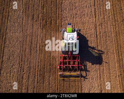 Luftaufnahme eines grünen Traktors, der ein Feld pflügt und Spuren auf dem Feld hinterlässt Stockfoto