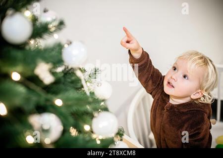 Süßer kleiner Junge, der neben dem weihnachtsbaum steht und mit dem Finger zeigt Stockfoto