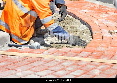 Ein maurermeister legt orange Pflasterplatten um einen Kreisverkehr auf der Straße. Stockfoto