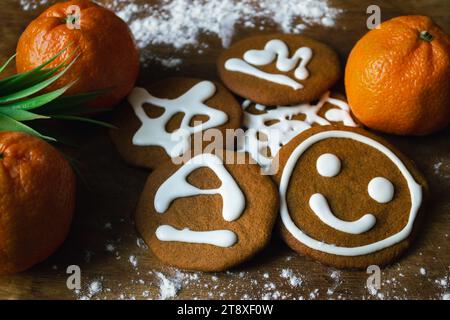 Süße Lebkuchenkekse, bedeckt mit weißer Glasur mit verschiedenen Mustern, umgeben von Mandarinen und einem Teil einer grünen Pflanze auf einem Brett mit Mehl Stockfoto