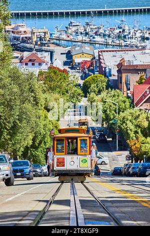 Trolley mit Touristen, die am Geländer halten, während die Leute am sonnigen Tag den Berg vom Hafen weg fahren Stockfoto
