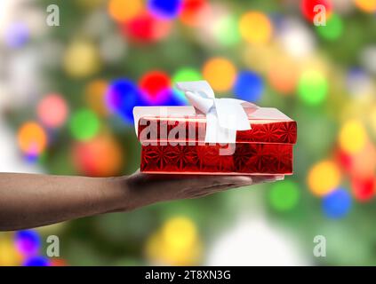 Hand eines Afro-Mannes, der Geschenkbox über Weihnachtsbaumhintergrund hält. Stockfoto