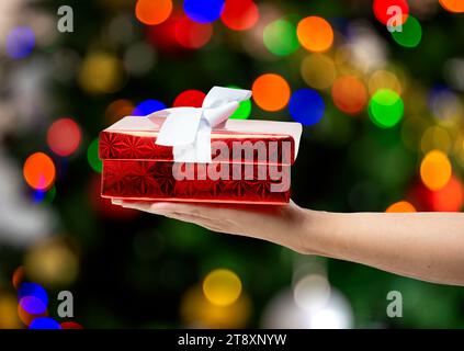 Hand eines Mannes, der Geschenkbox über Weihnachtsbaumhintergrund hält. Stockfoto