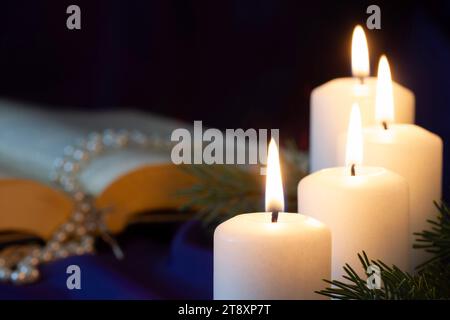 Vier brennende Adventskerzen mit offener Bibel und Rosenkranz im Hintergrund, religiöses Symbolkonzept Stockfoto