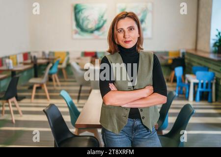 Porträt einer lächelnden kleinen Geschäftsfrau, die in Küchenuniform in ihrem gemütlichen Restaurantsaal gekleidet ist. Erfolgreiche Menschen, harte Arbeit, Verbraucher, Café Stockfoto