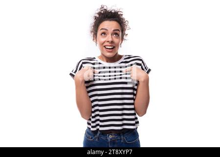 Junge traumhafte, gut gepflegte lockige Frau mit schwarzen Haaren in einem Sommer gestreiften T-Shirt Stockfoto