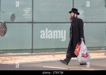 Ein orthodoxer jüdischer Mann, wahrscheinlich aus der Satmar-Gruppe, trägt Einkaufstaschen und läuft an einer Baustelle in Brooklyn, New York, vorbei. Stockfoto