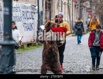 2. Dezember 2022-Bukarest Rumänien- Weihnachtslieder auf der Straße mit einem Kollegen in Bärenfell gekleidet mit großen roten Quasten tanzend, während sie singen. Stockfoto