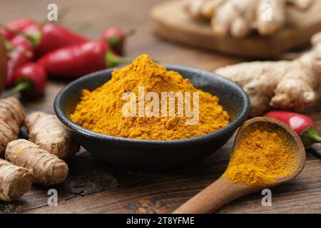 Schüssel Curcuma zu Pulver gemahlen und ganze Kurkuma Wurzeln. Rote Chilischoten und Ingwerwurzeln auf dem Hintergrund. Zutaten zum Kochen und Ayurveda Stockfoto