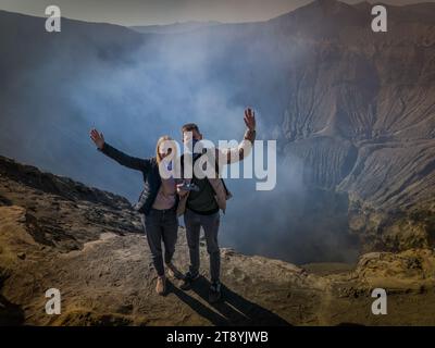 Junges Paar am Rand des aktiven Vulkankraters Bromo, Ost-Java, Indonesien. Panoramaansicht des Rauchgasdampfes aus dem Krater Stockfoto