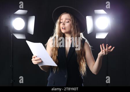 Schöne Schauspielerin mit Drehbuch auf dunklem Hintergrund Stockfoto