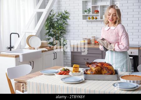 Schöne junge Frau mit leckerem gebackenem truthahn am Tisch in der Küche. Thanksgiving-Feiertag Stockfoto