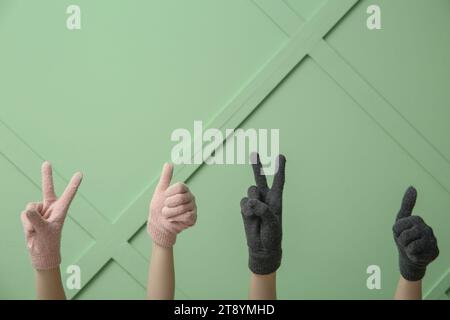 Frauen in warmen Handschuhen zeigen Daumen nach oben und Siegesgesgestik an der farbigen Wand Stockfoto