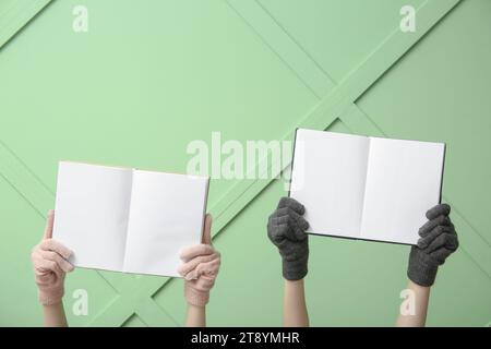 Weibliche Hände in warmen Handschuhen mit leeren offenen Büchern gegen Farbwand Stockfoto