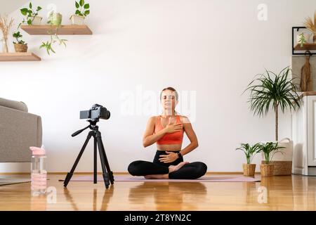 Yogacoach-Aufnahme von Meditationsübungen. Frau, die Atemübungen und Meditationen in Lotusstellung macht. Stockfoto