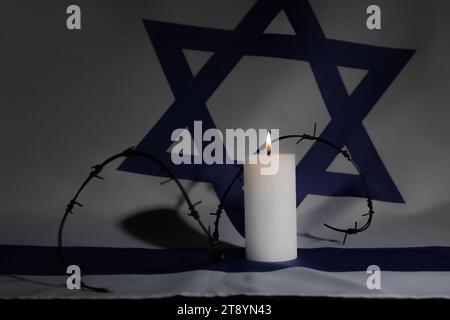 Brennende Kerze mit Stacheldraht auf der Flagge Israels. Internationaler Holocaust-Gedenktag Stockfoto