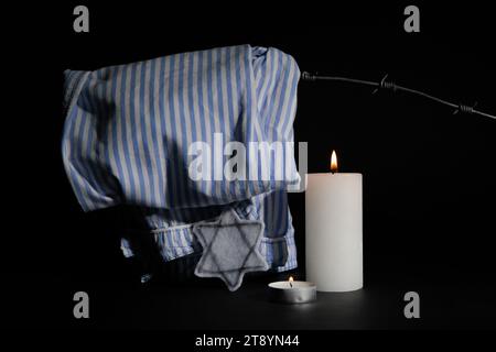 Brennende Kerzen mit jüdischem Abzeichen und Gefangenenuniform auf dunklem Hintergrund. Internationaler Holocaust-Gedenktag Stockfoto